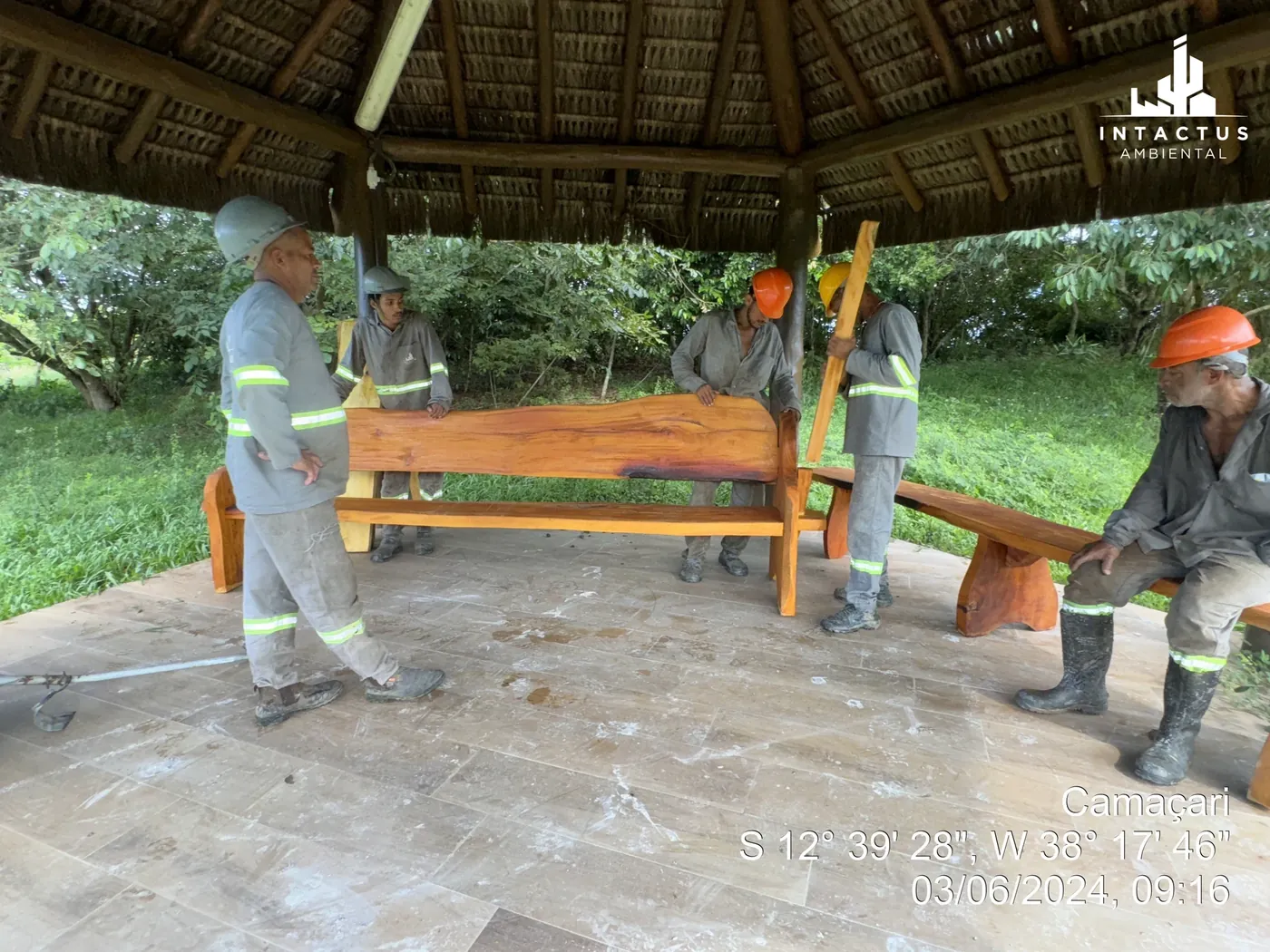 Equipe trabalhando com um banco de madeira sob a cobertura do Projeto Florescer