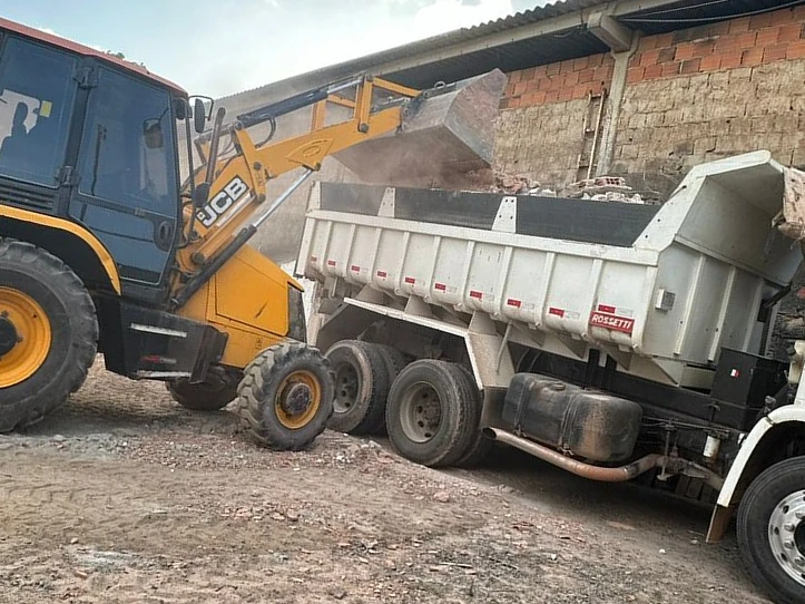 Retroescavadeira junto a caminhão basculante durante operação de movimentação de materiais