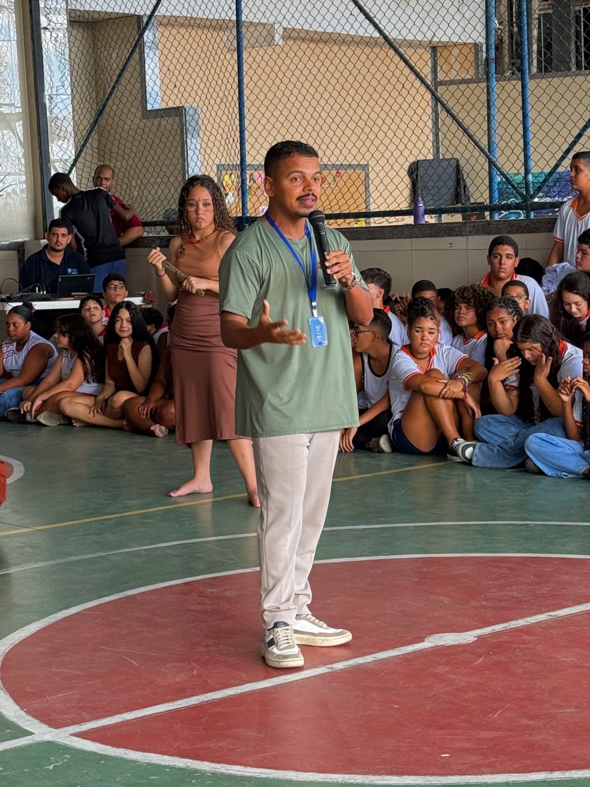 Palestrante fala ao microfone para estudantes em uma escola pública.
